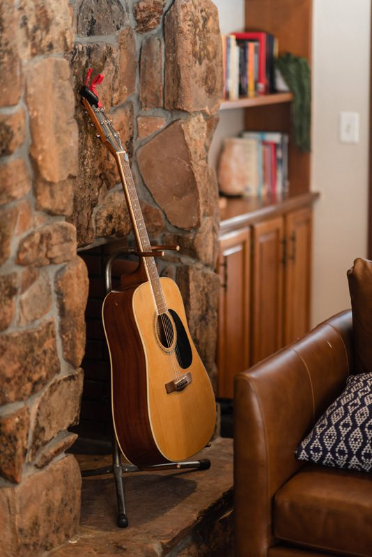 Acoustic guitar resting beside stone fireplace