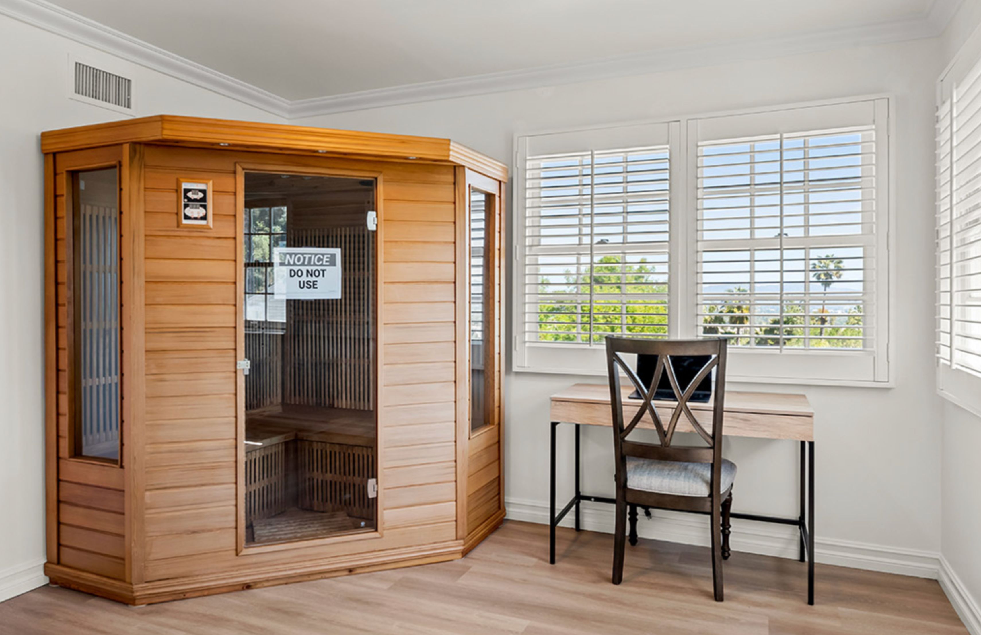 A room with a wooden sauna, desk, and large windows.