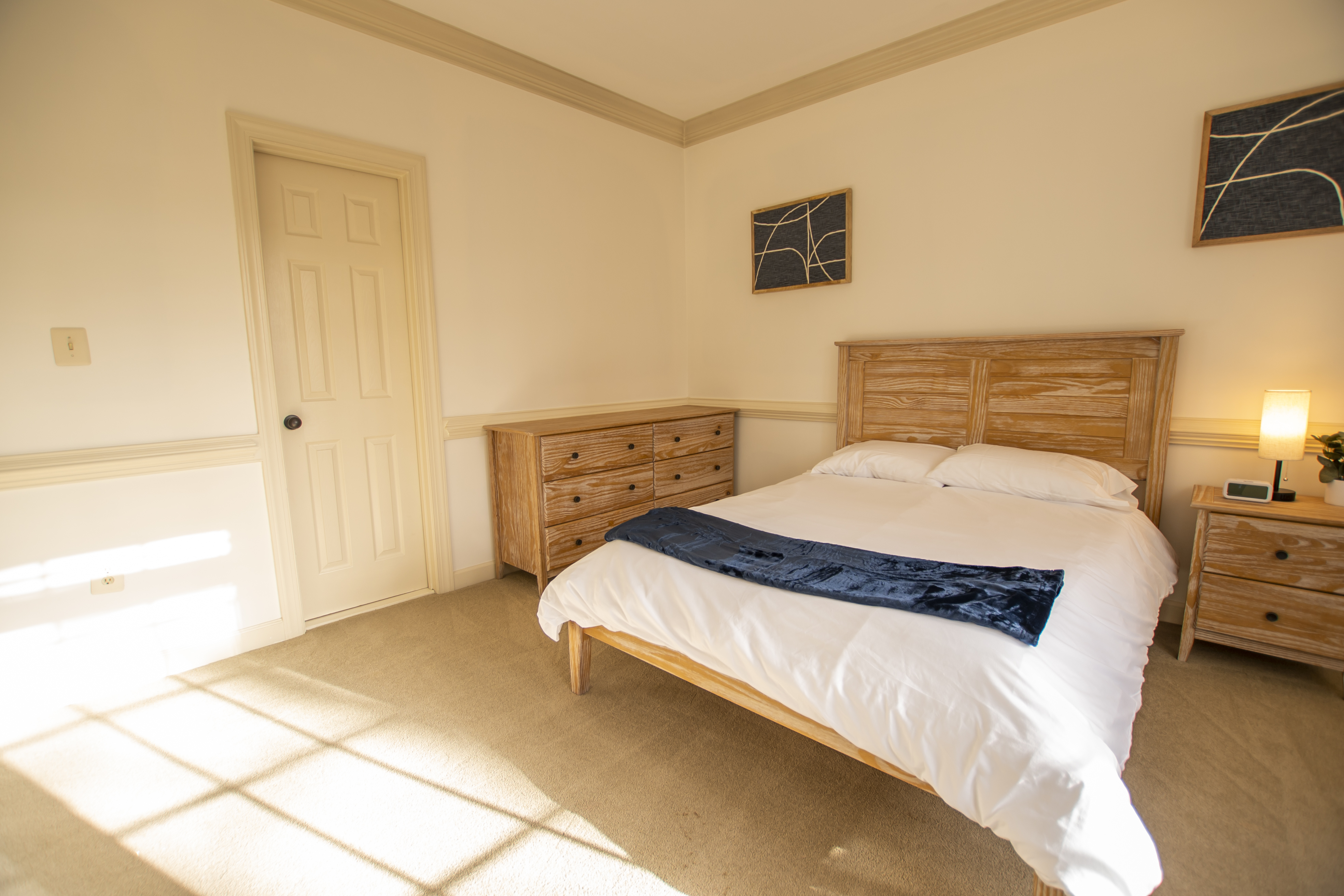 Bright bedroom with queen bed and wood furnishings.