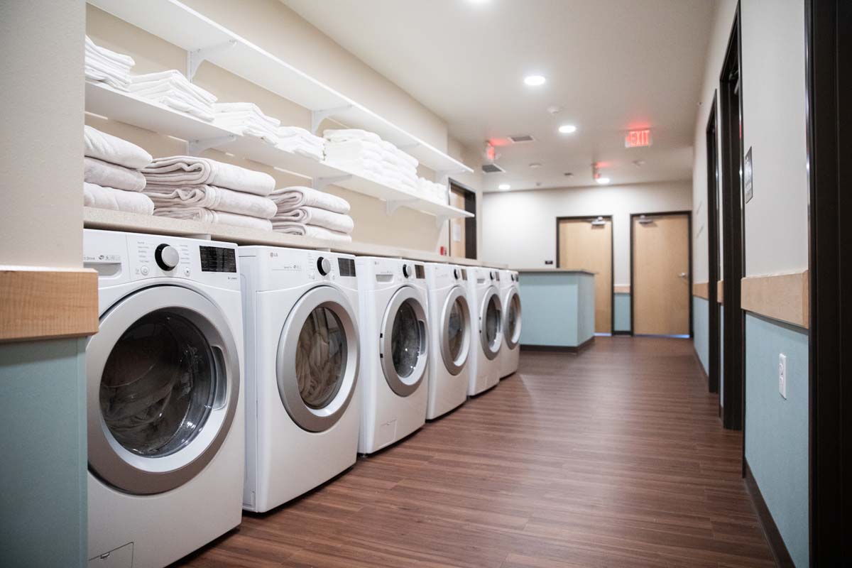 Row of washers and dryers with folded towels on shelves