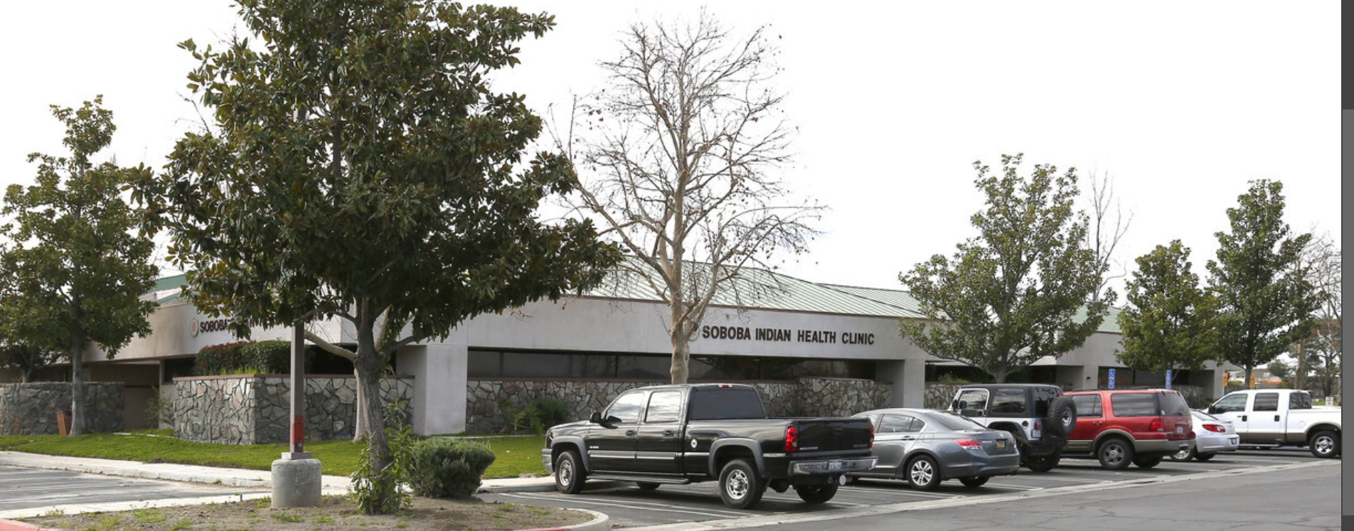 Front view of the Soboba Indian Health Clinic, with a well-maintained parking area surrounded by mature trees.