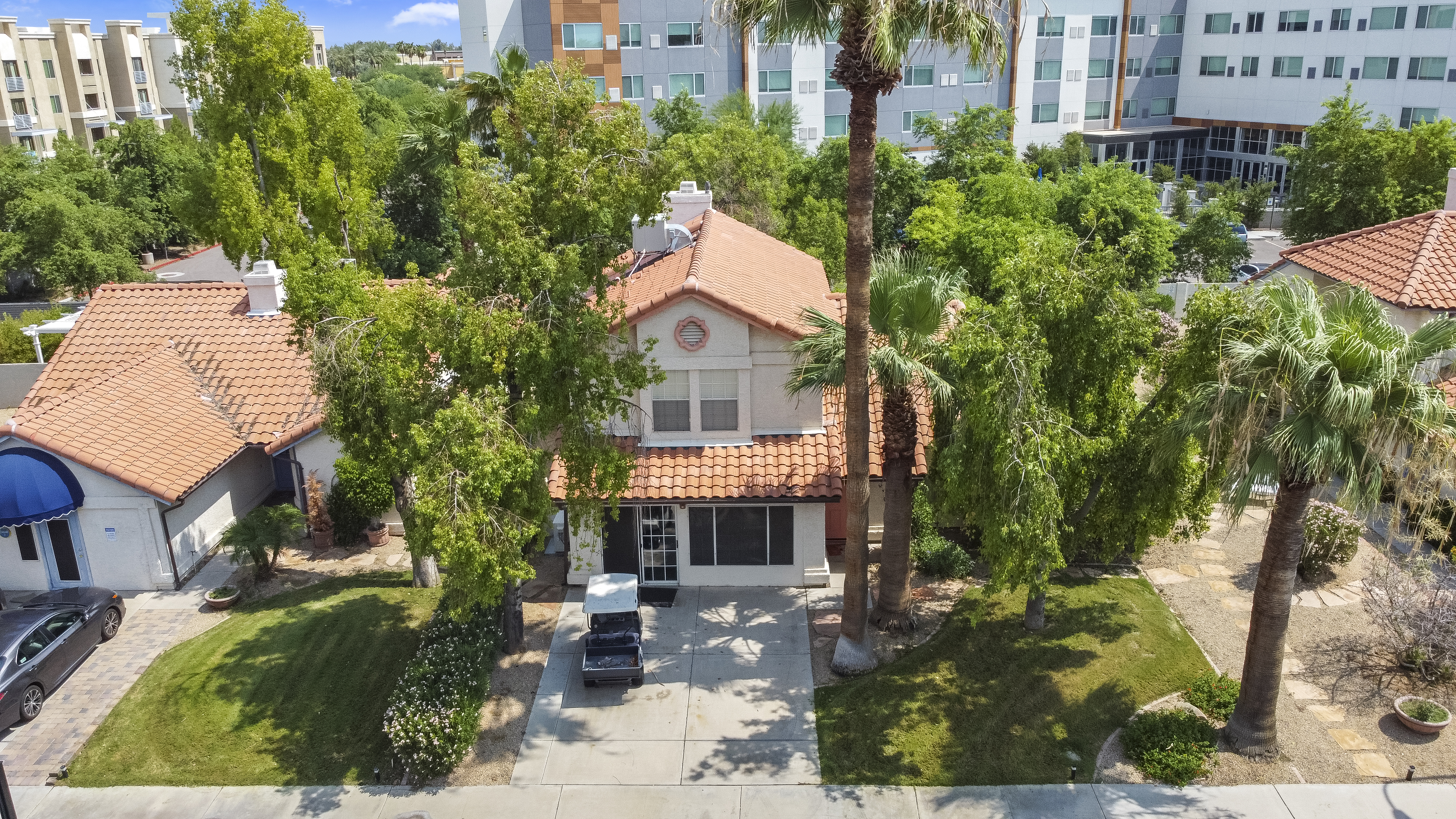 Two-story house with a red tile roof, around palm trees,