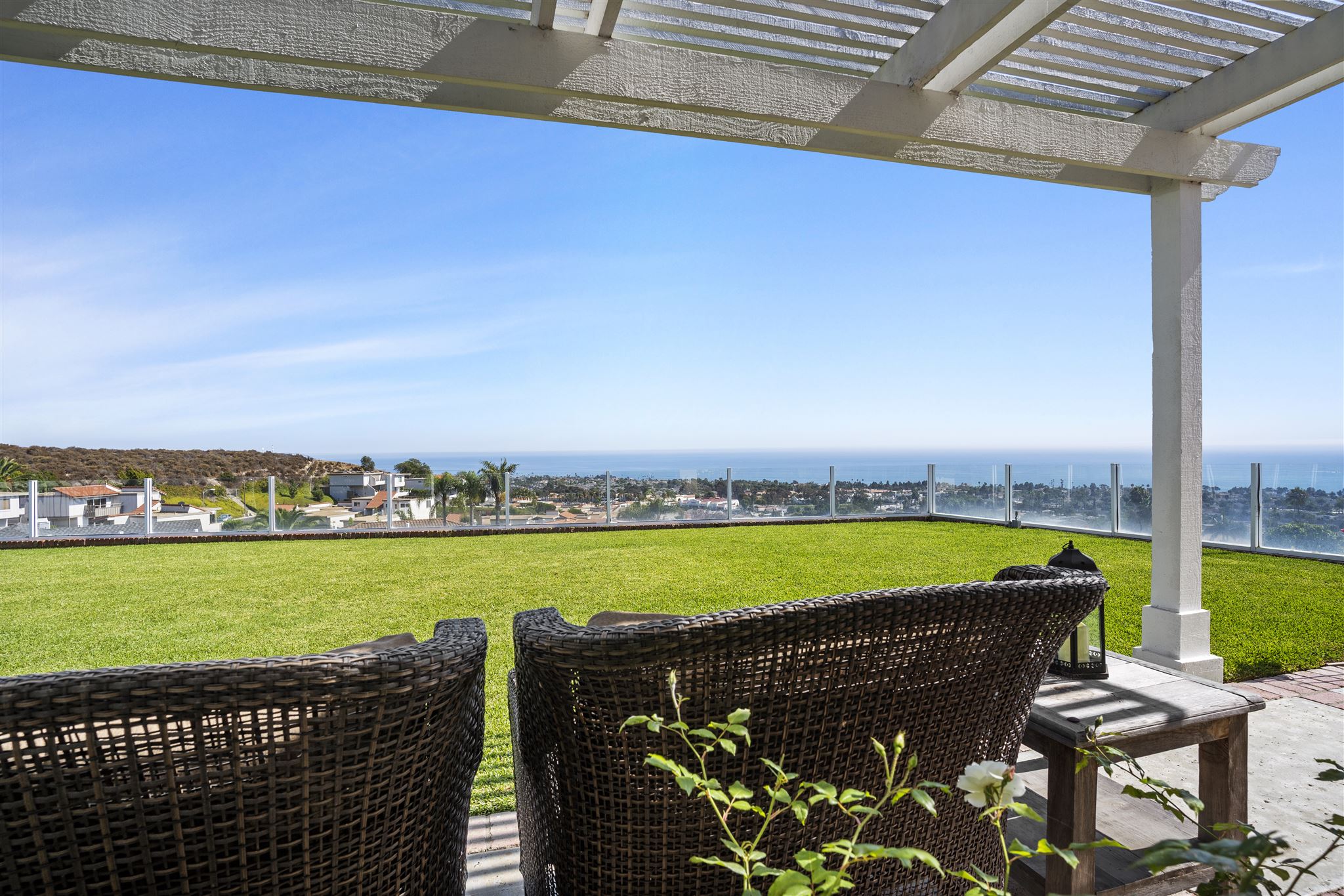 Outdoor seating area with ocean views, green grass, and glass railing.