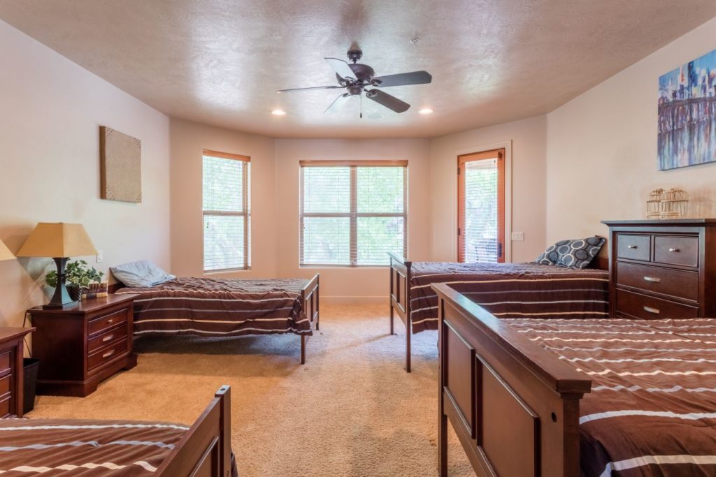 Shared bedroom with four wooden beds and large windows.