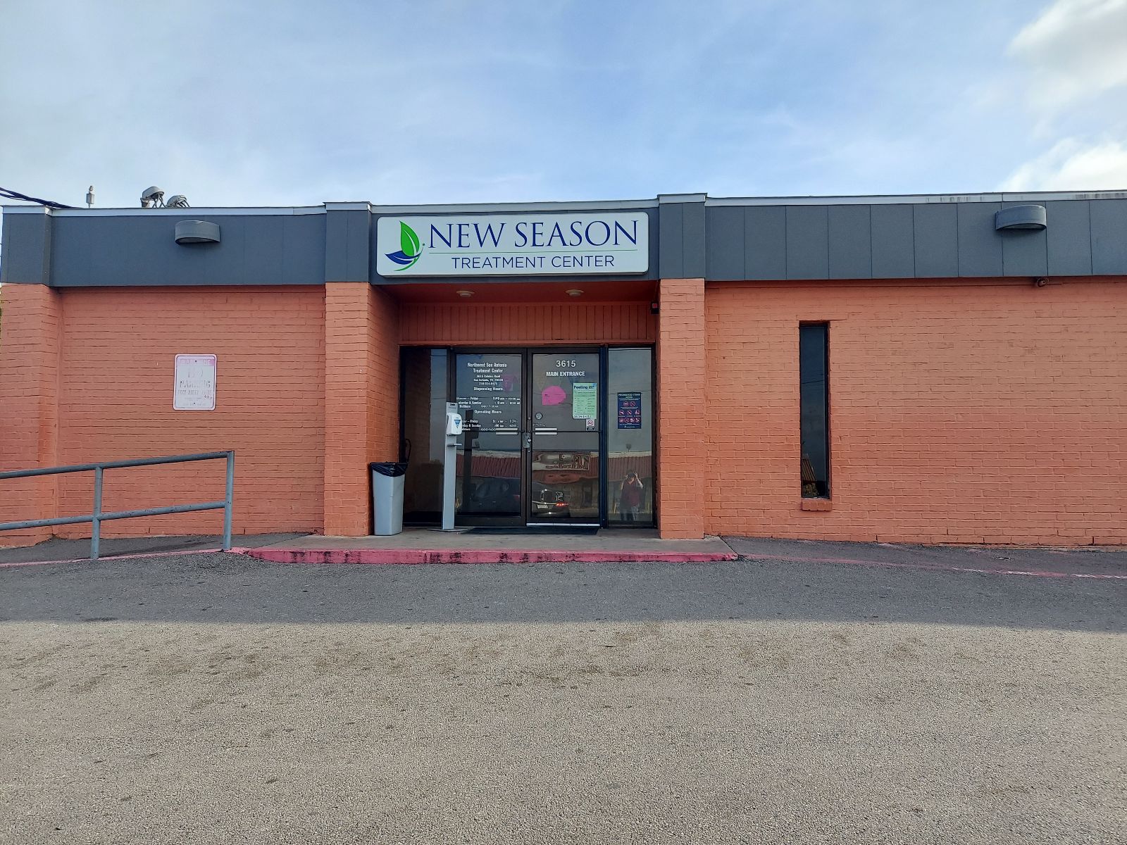 Glass door entrance with New Season sign and orange brick wall