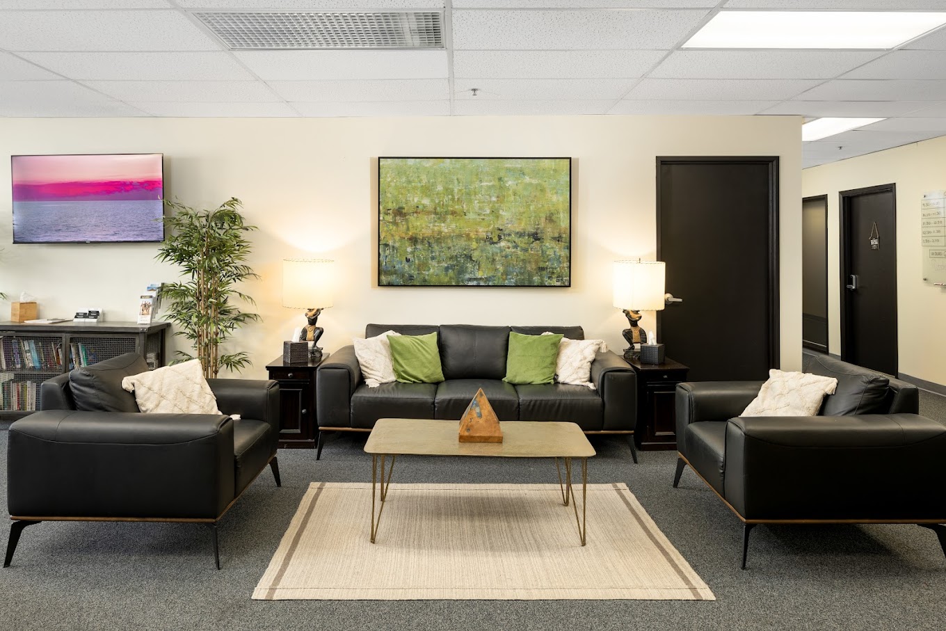 Group therapy room with black chairs and beige walls.