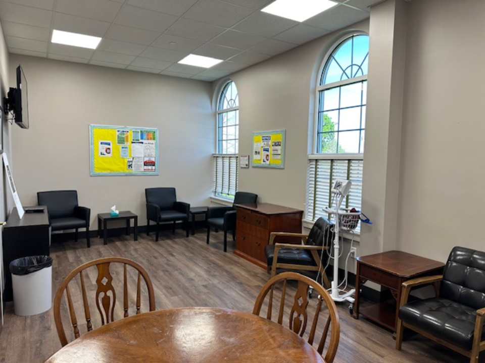 BrightView Health patient room with chairs, round table, medical equipment, bulletin boards, and tall arched windows