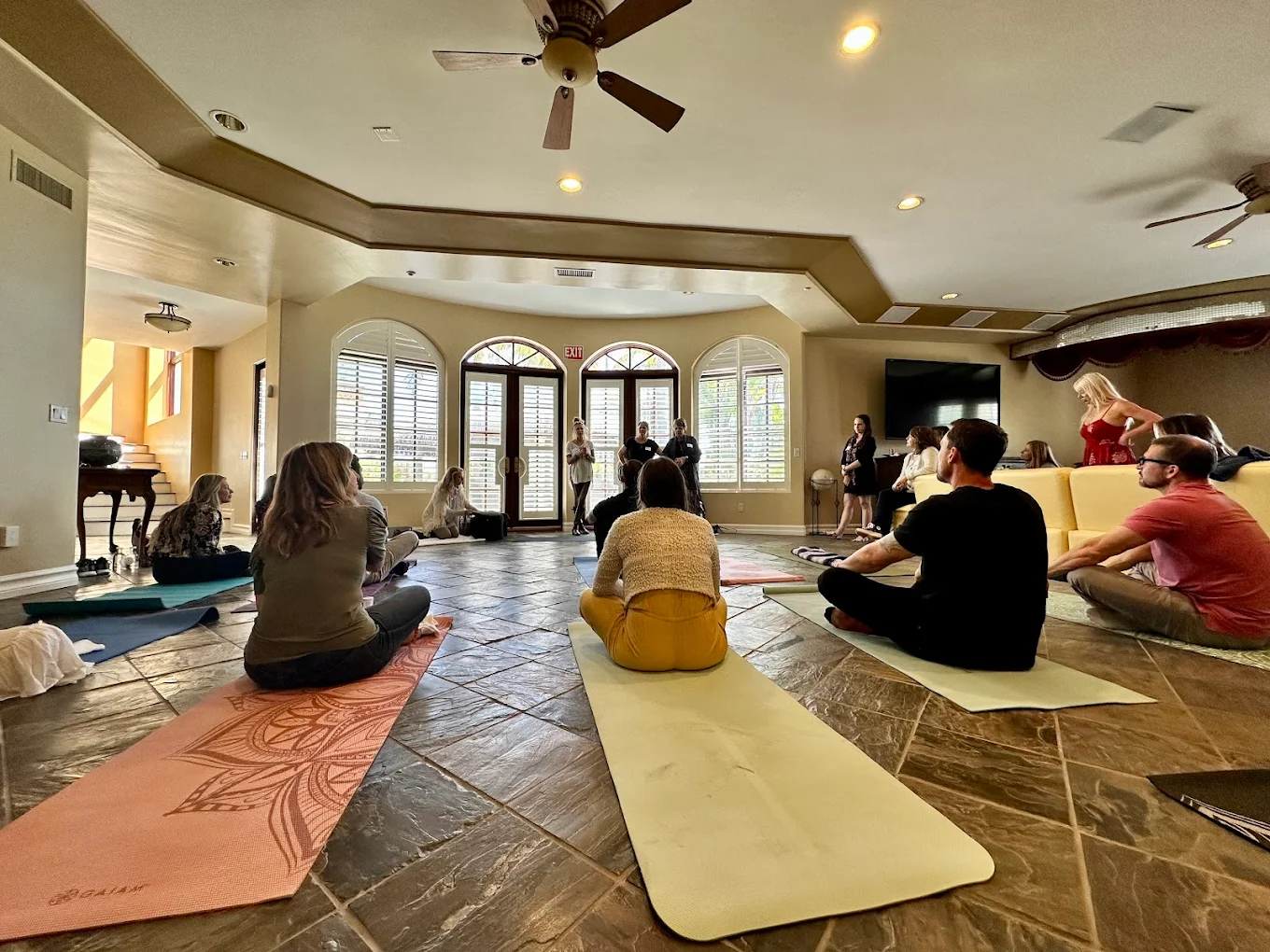 People seated on yoga mats in a large sunlit room
