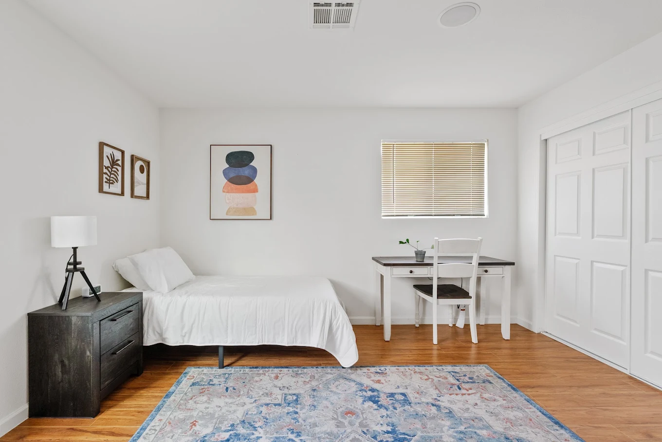 Bright bedroom with single bed, desk, rug, and wood flooring