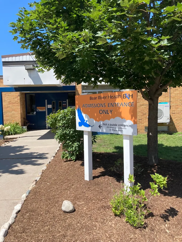 Sign outside admissions entrance under a tree