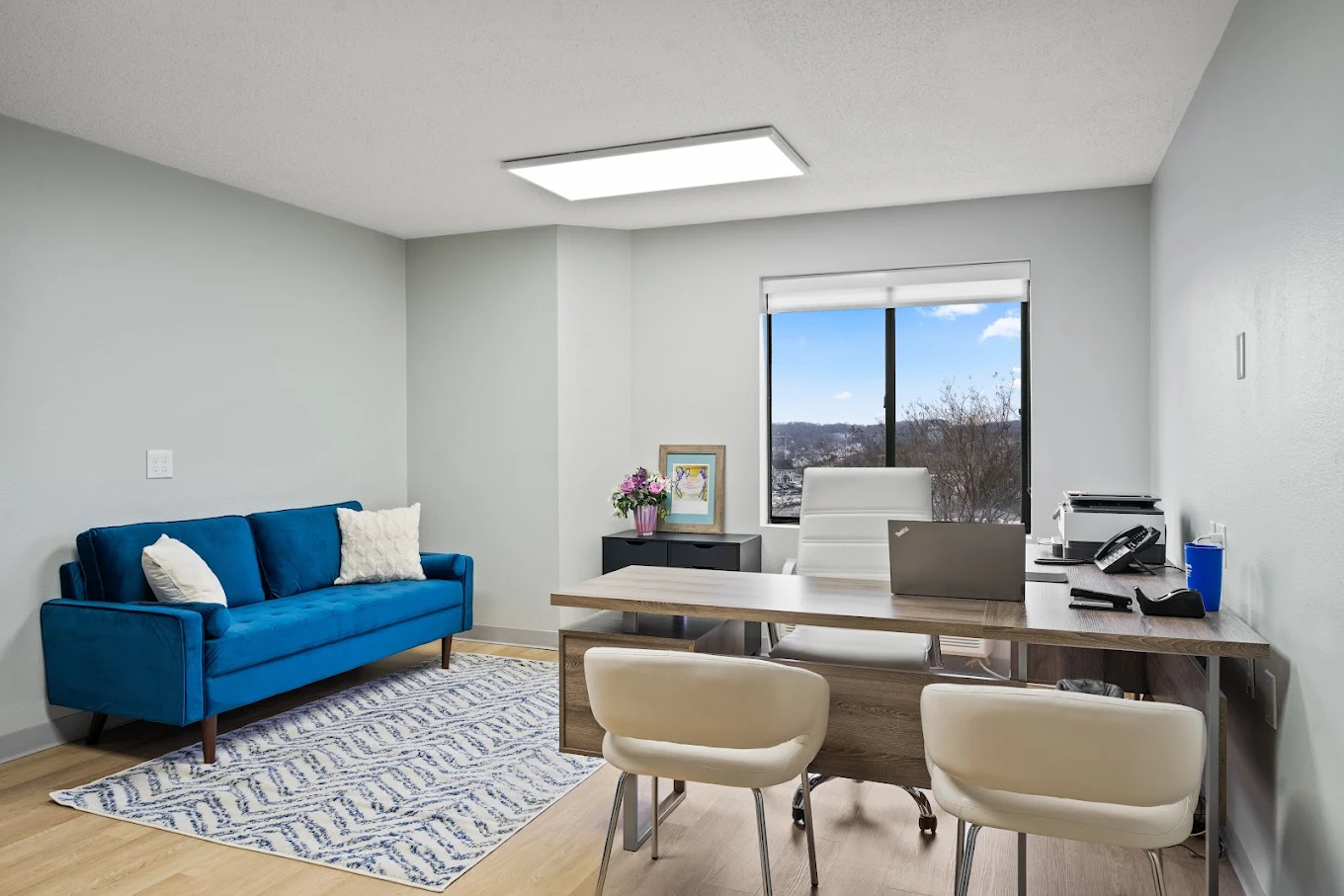 Bright office with large window, executive desk, and blue couch for guests