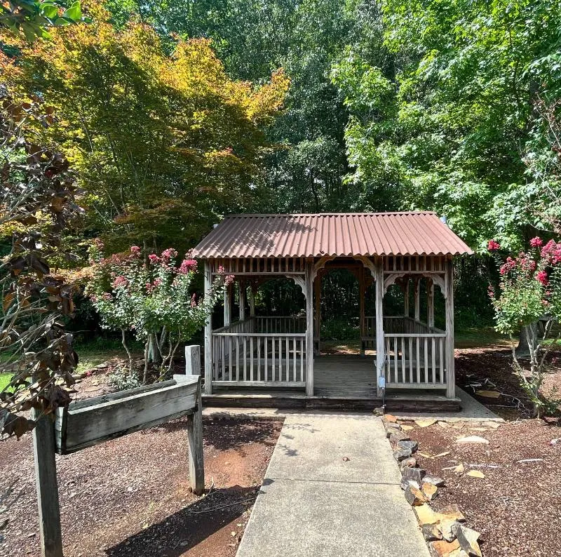 Wooden gazebo surrounded by trees and flowering plants