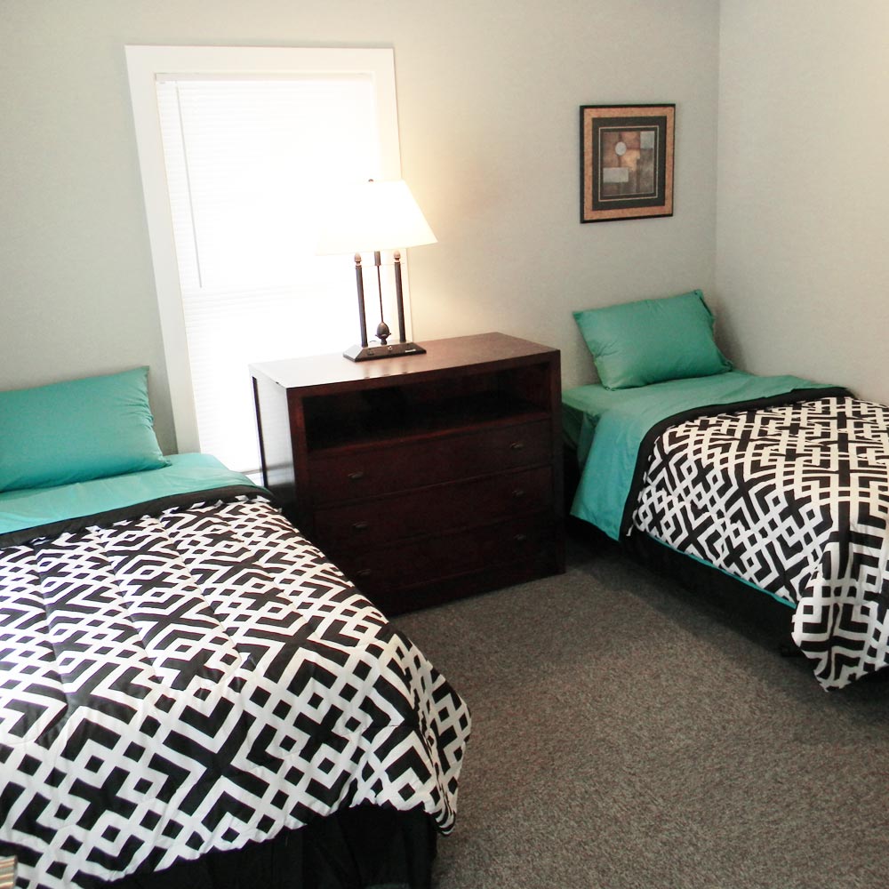 Two twin beds with teal pillows and black patterned bedding