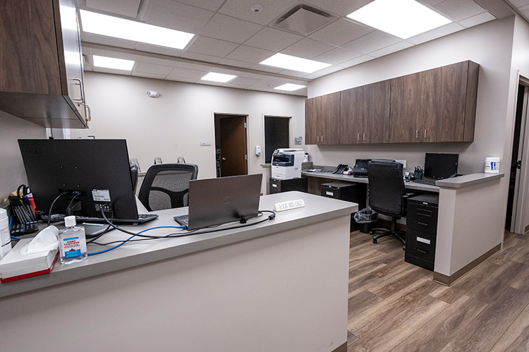 Staff workstation with computers, office chairs, wraparound counters, printer, storage cabinets, and wood-look flooring