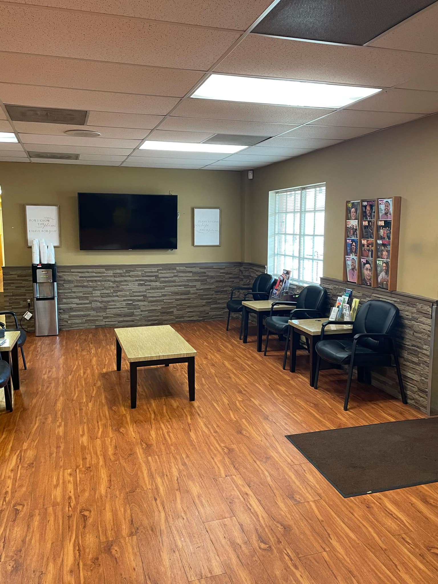 Waiting area with TV, wood flooring, and chairs against beige wall
