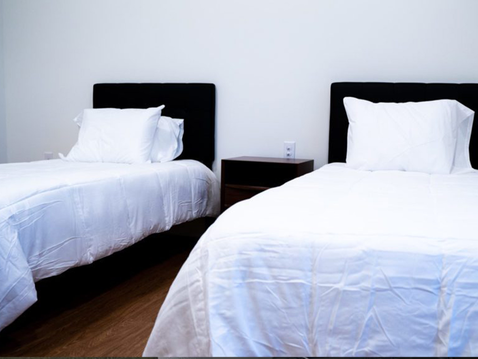A bedroom with two beds, white bedding, and a nightstand