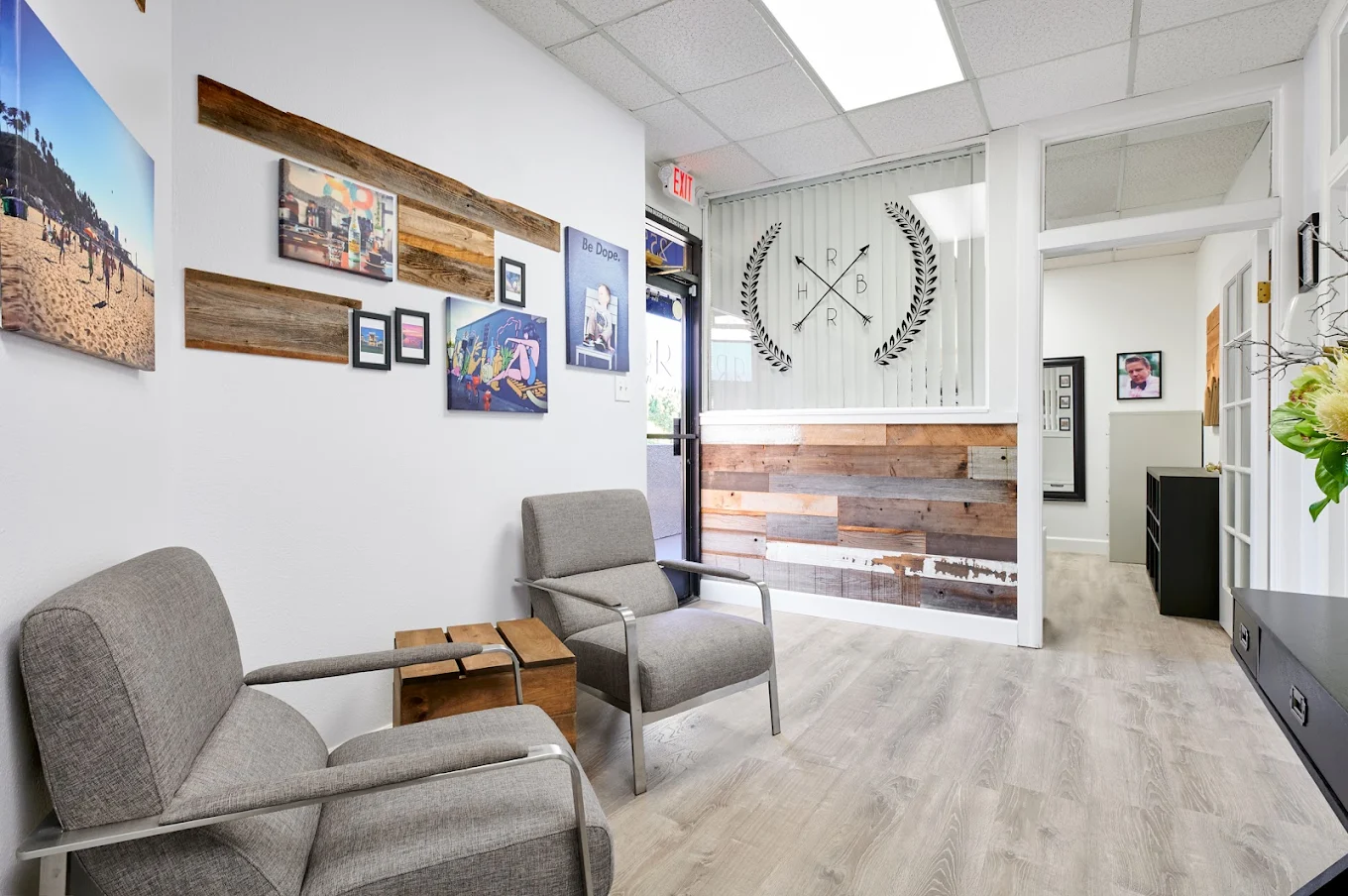 Welcoming lobby with grey chairs, wooden accents, beach-themed artwork, and R&R Recovery logo on glass wall