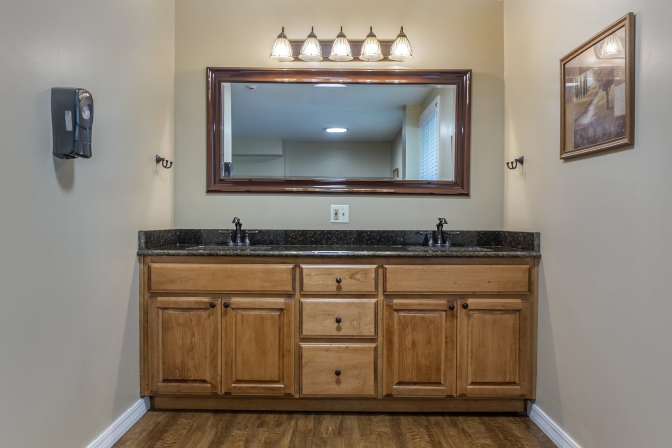 A well-lit bathroom with a double-sink vanity, a large framed mirror, and wooden cabinetry.
