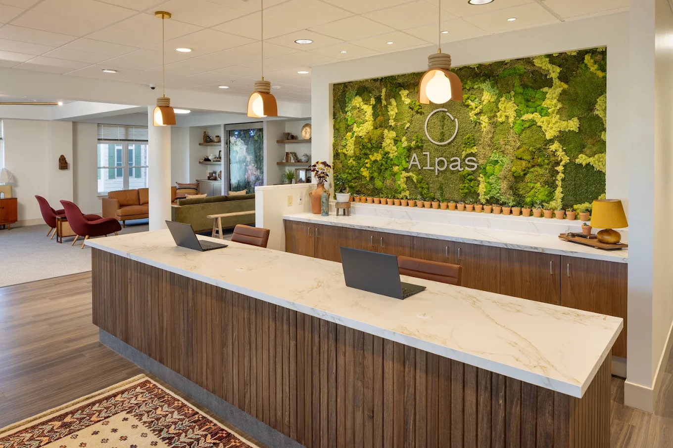 Reception desk with pendant lights and a large green Alpas wall display.