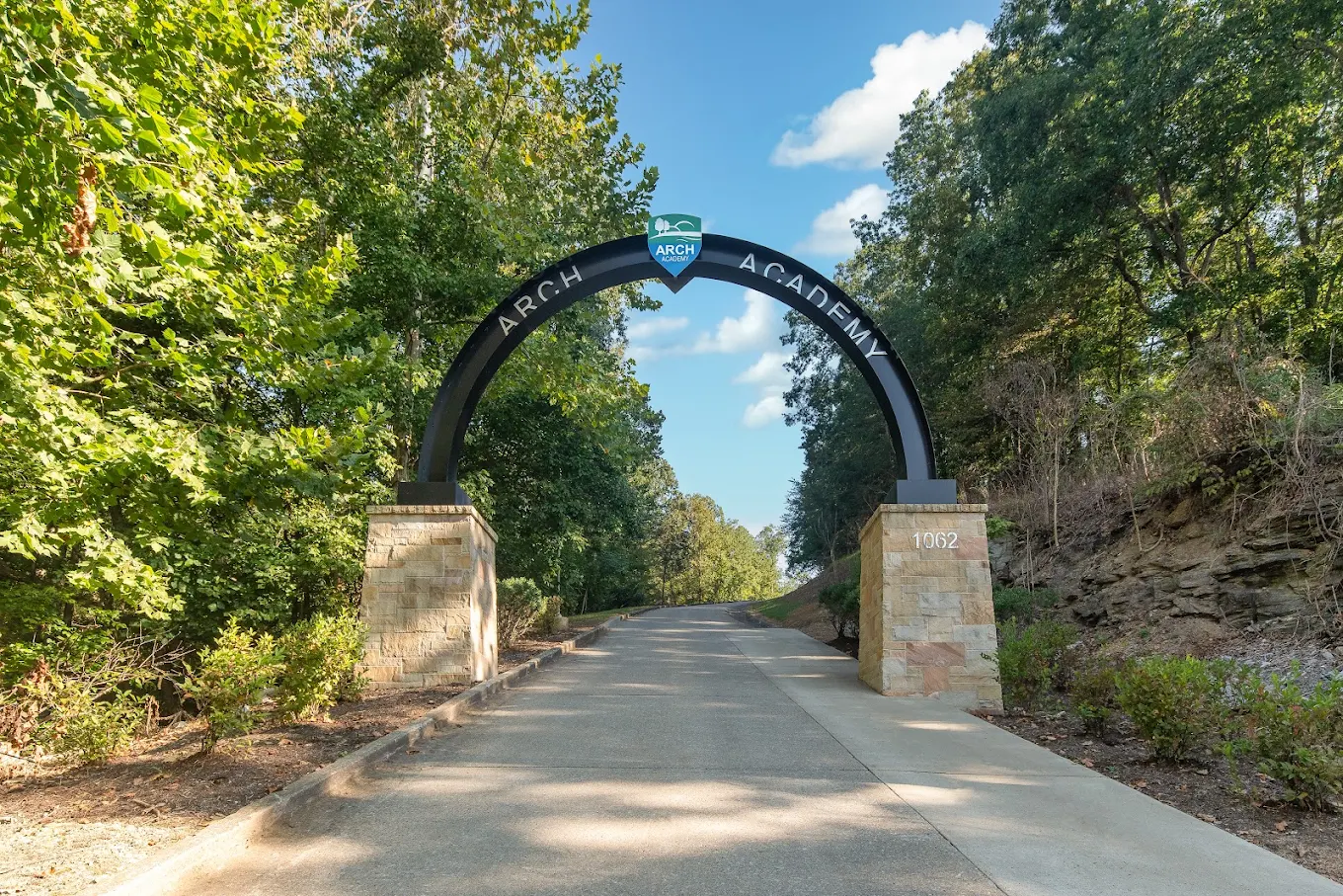 Tree-lined entrance road with ARCH Academy archway sign.