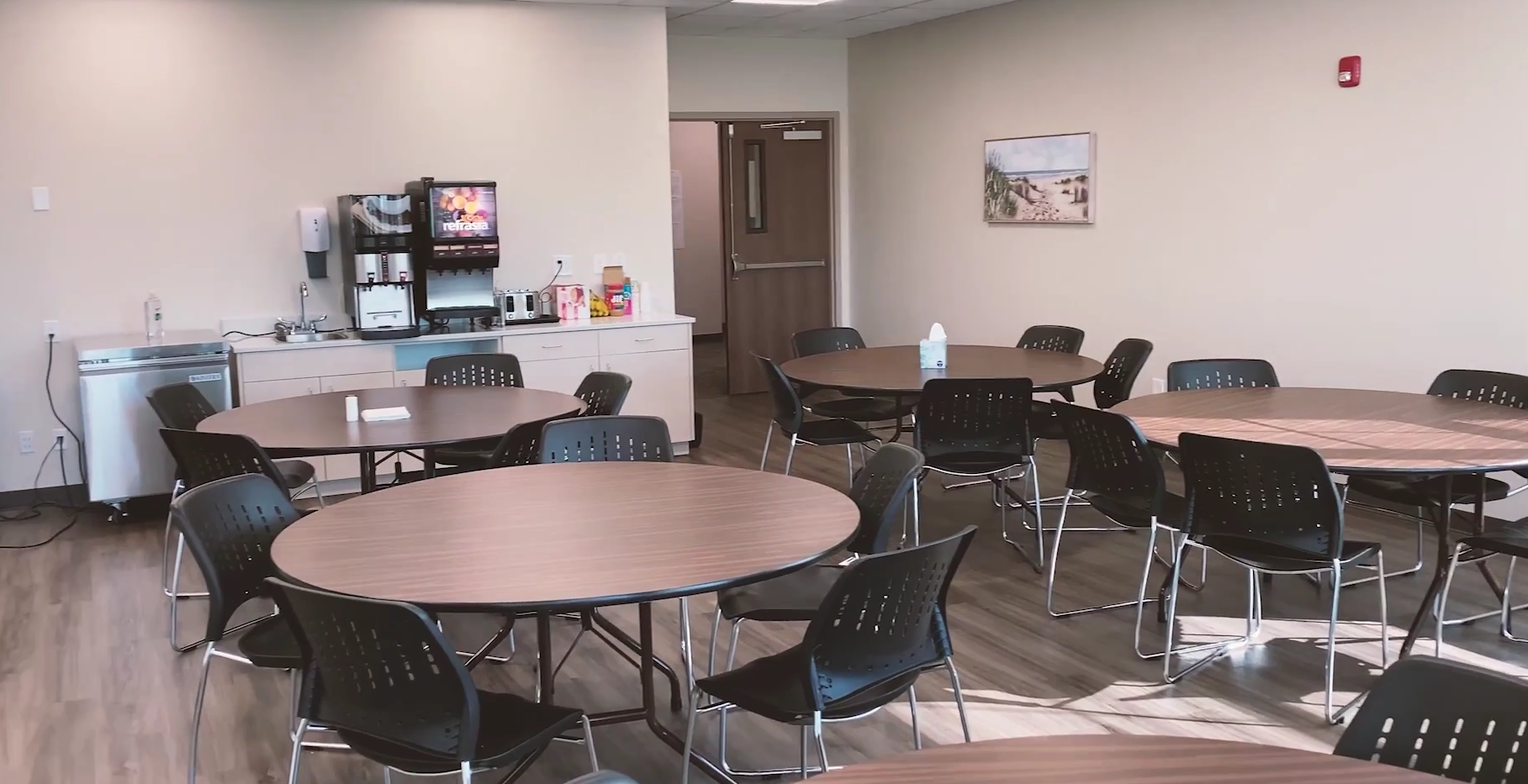 Shared dining room with round tables, chairs, and beverage station