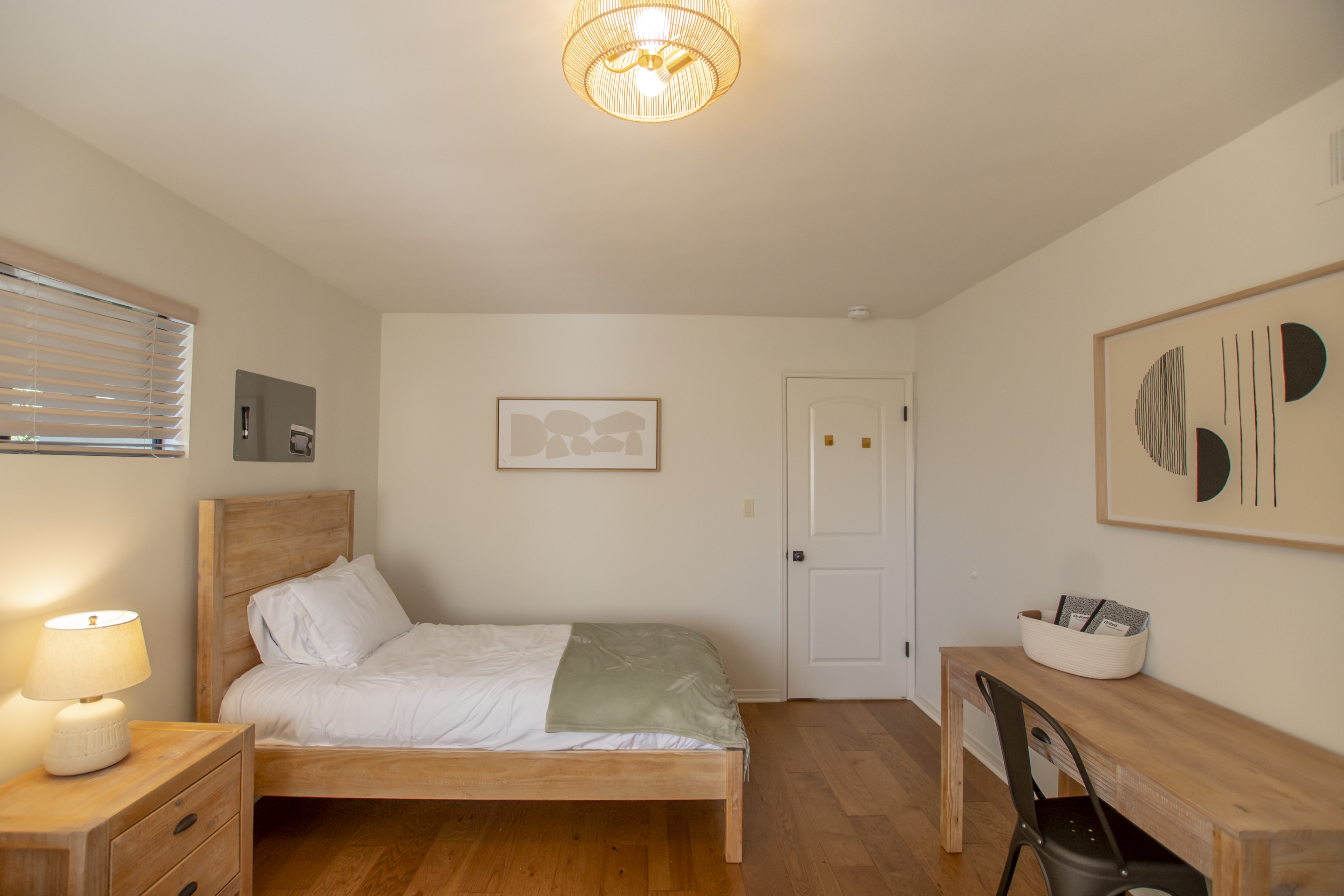 A private bedroom with a wooden bed, desk, and neutral decor.