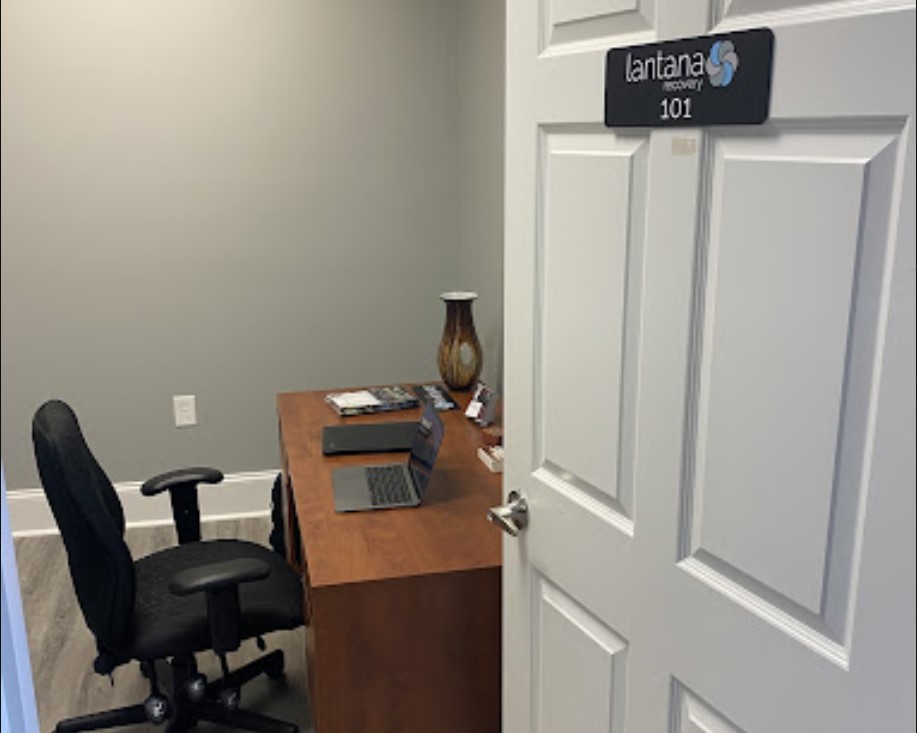 A small office with a wooden desk, black chair, and an open laptop
