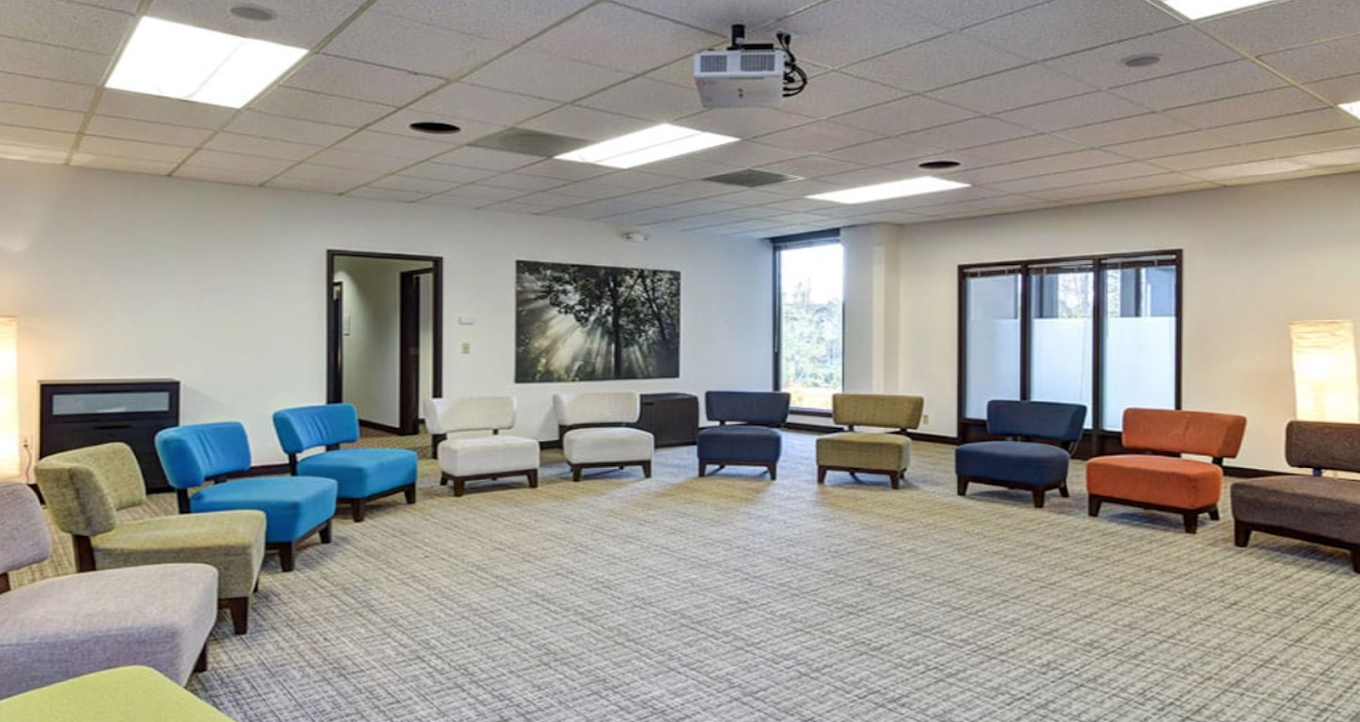 Large therapy room with circle of colorful, cushioned chairs and neutral walls, designed for group sessions
