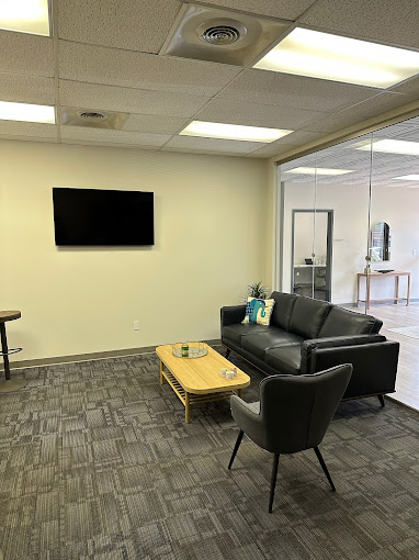 A modern waiting area with a black couch, armchair, and mounted TV.