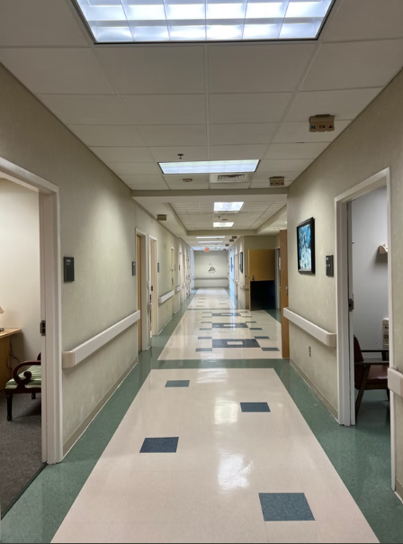 Long hallway with patient rooms on each side, cream-colored walls, and patterned flooring