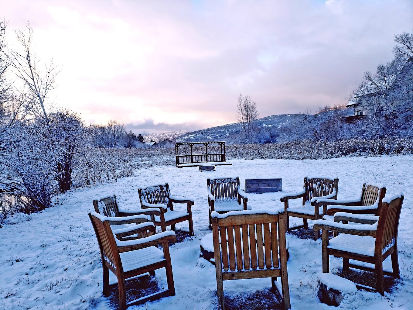 Wooden chairs around firepit in snowy landscape