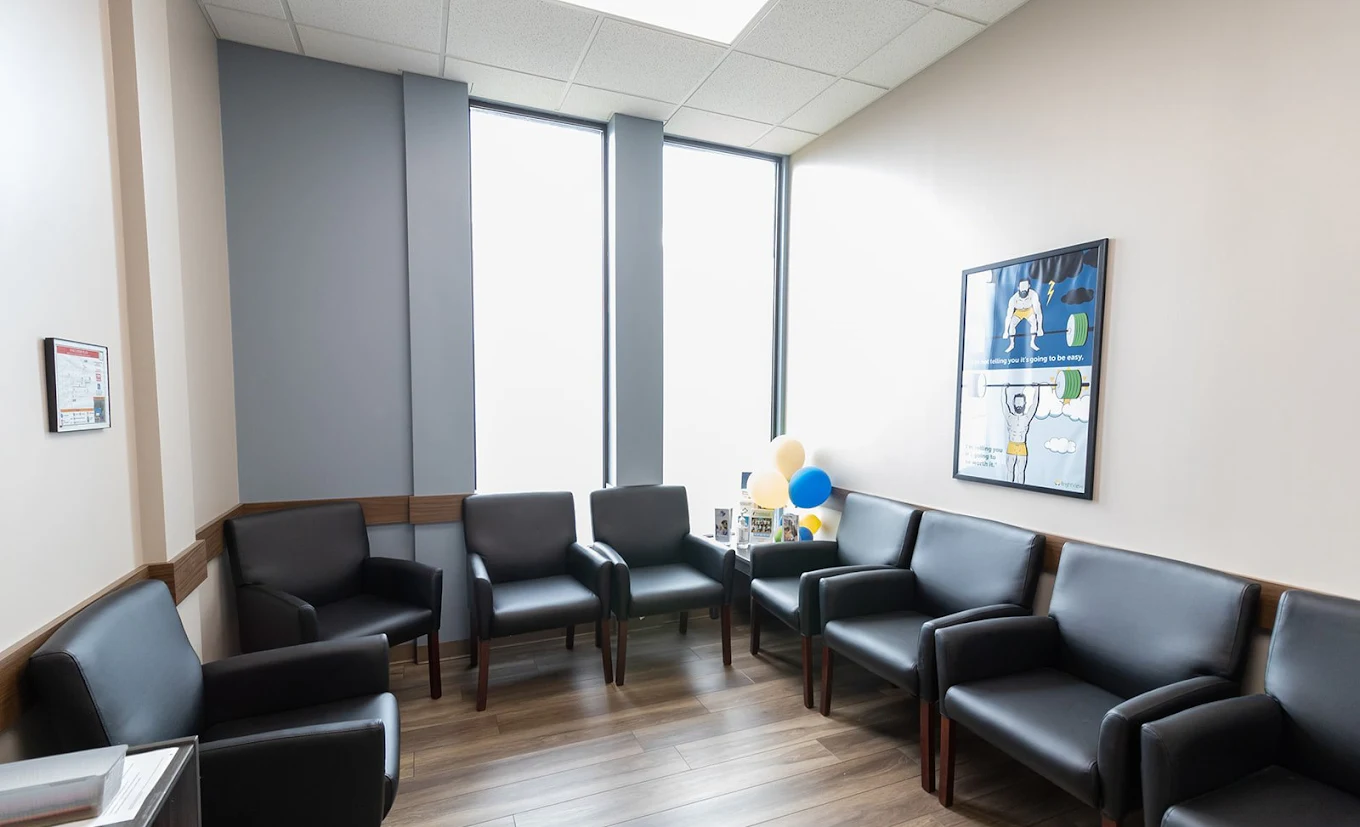 BrightView Health treatment area with cushioned black armchairs arranged around the room, tall windows, blue accent walls, wood-look flooring, and framed wall art