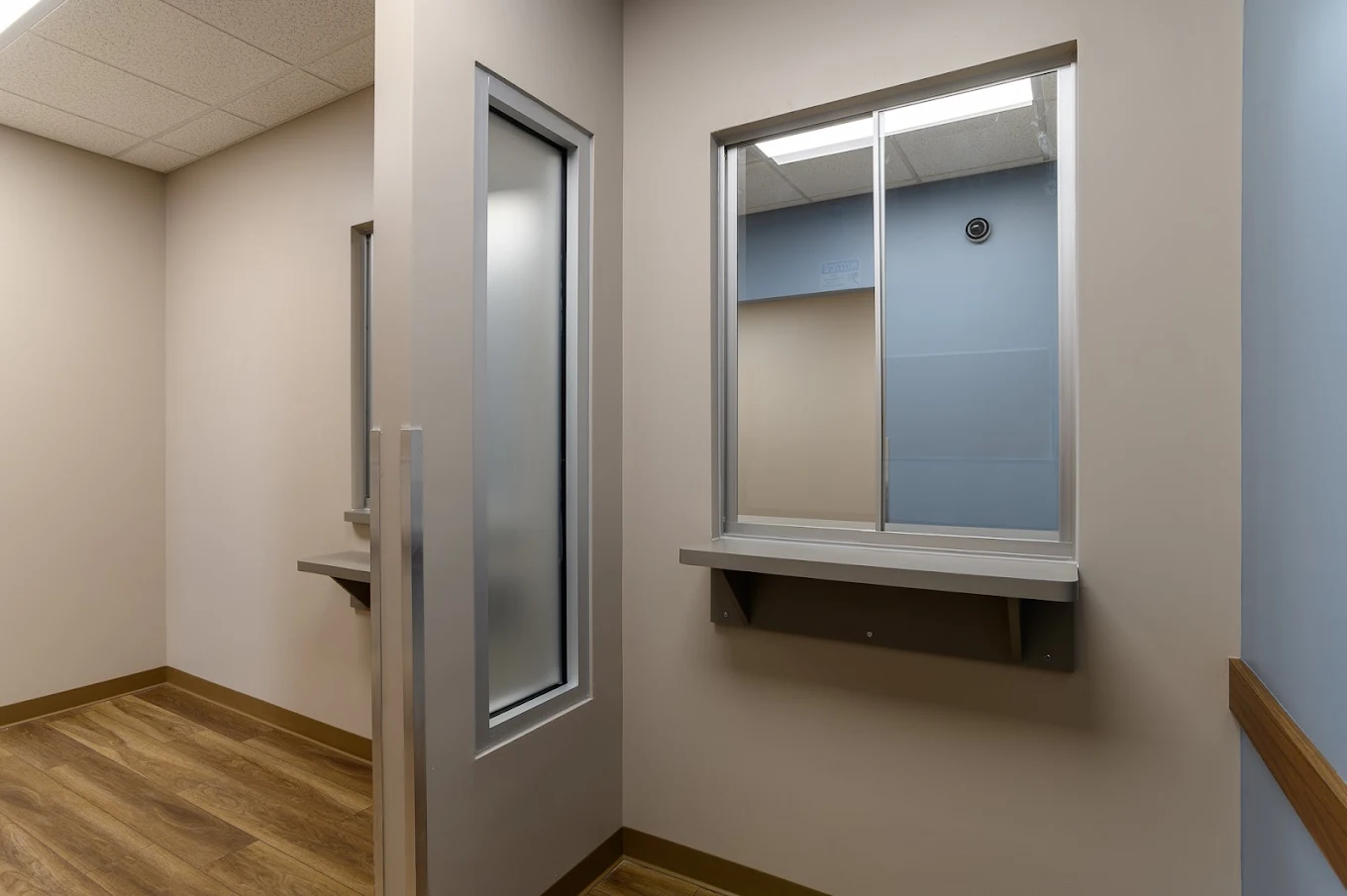 Interior medication dispensing area at BrightView Health with service windows, privacy partitions, beige walls, blue accent wall, and wood-look flooring