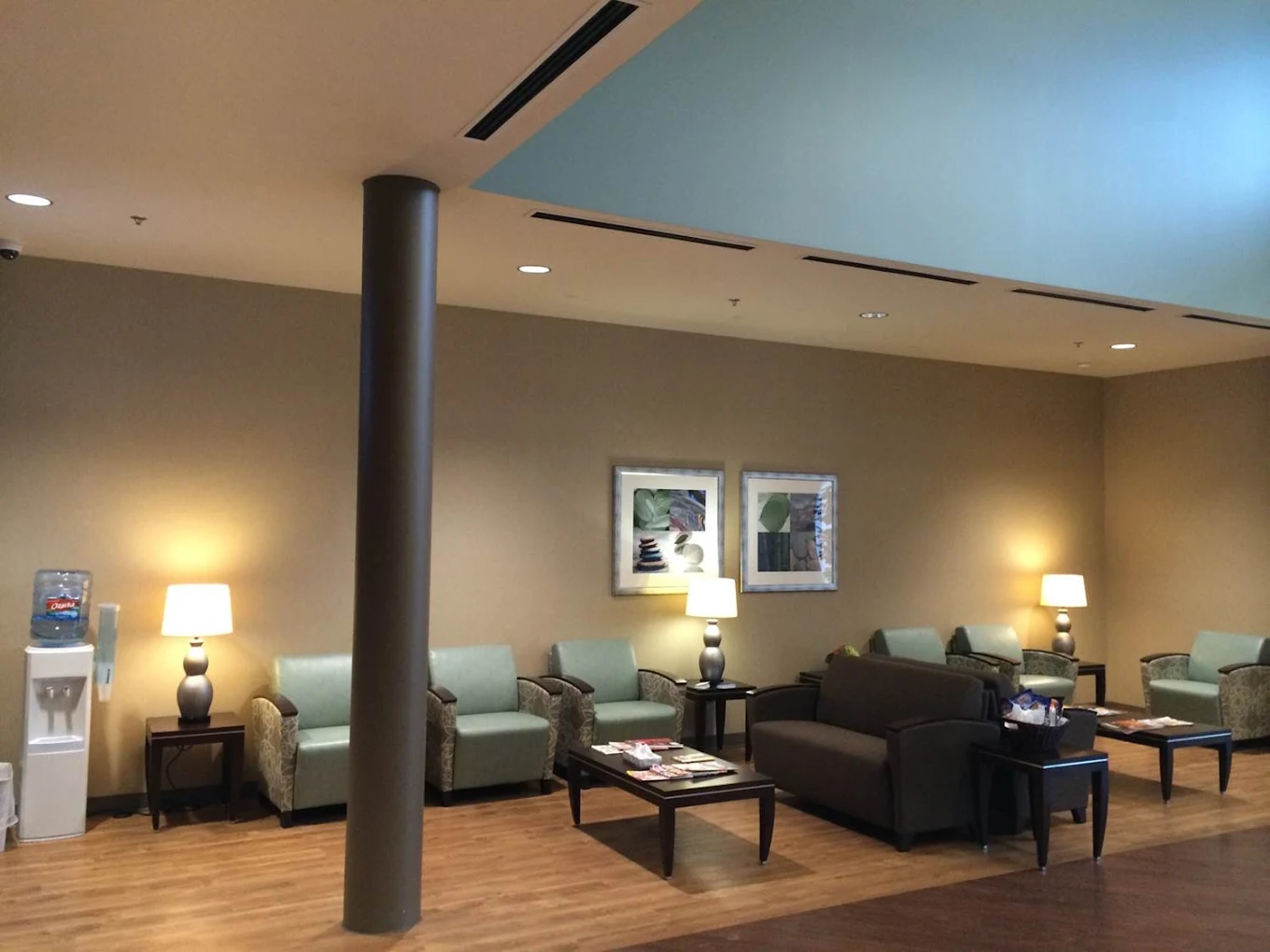 A warm and inviting living area with soft armchairs, side tables, and lamps arranged around coffee tables, creating a cozy space for relaxation.