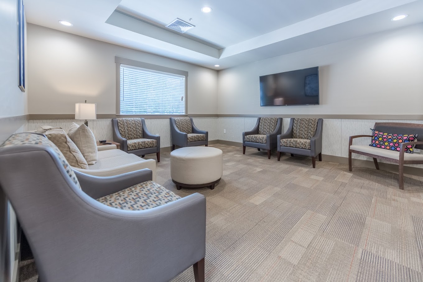 Modern waiting area with gray chairs, a TV, and soft lighting.