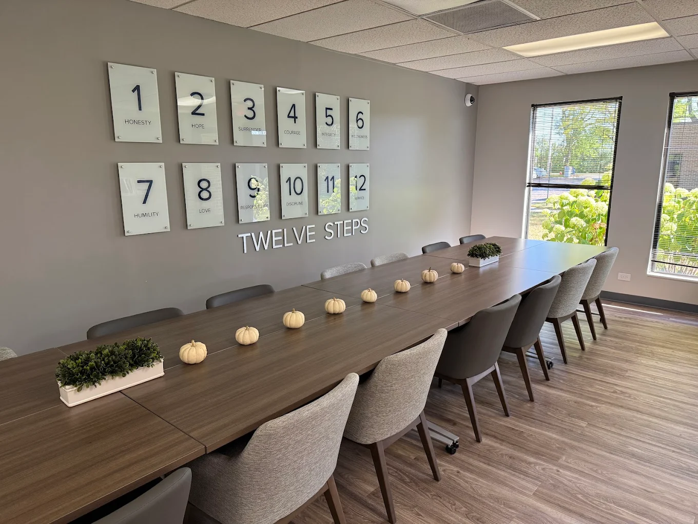 Long meeting table beneath a Twelve Steps wall display