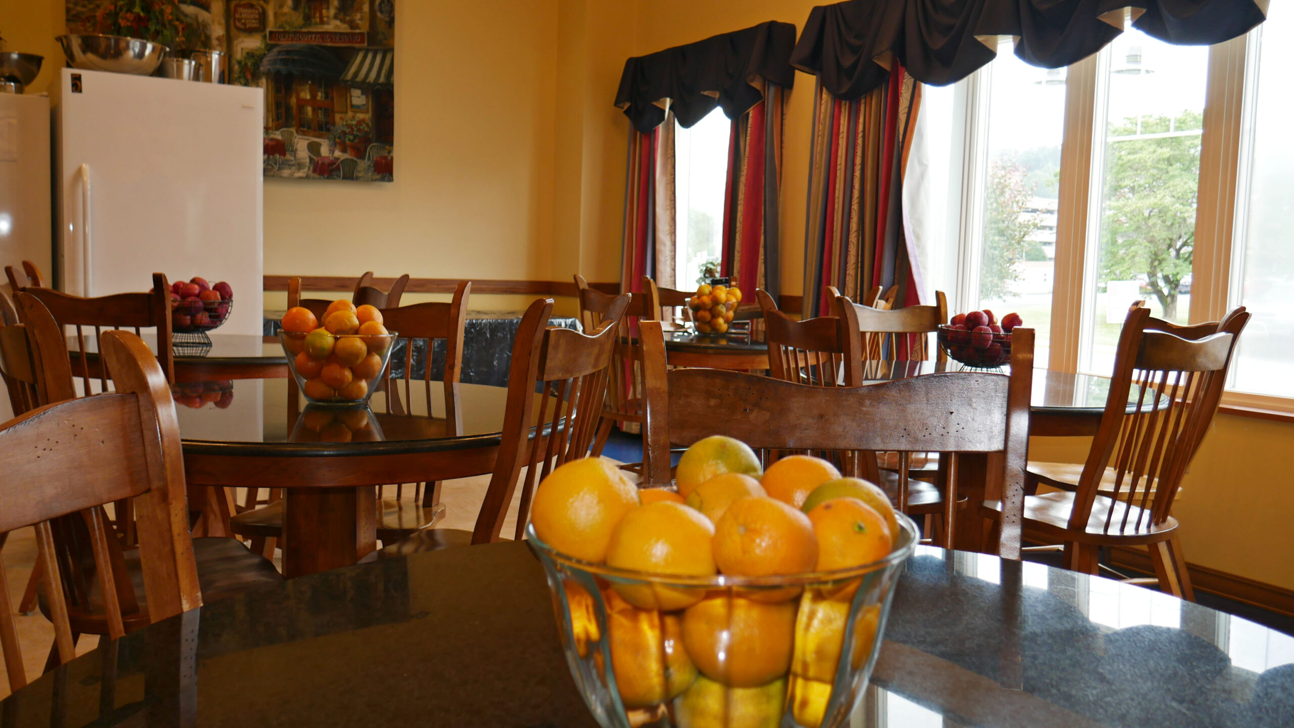 Dining tables with chairs and bowls of fresh fruit near large windows