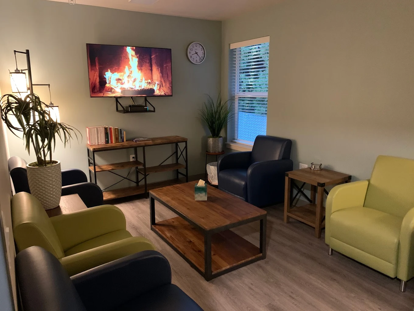 Cozy lounge with colorful armchairs, a coffee table, bookshelves, and a wall-mounted TV showing a fireplace