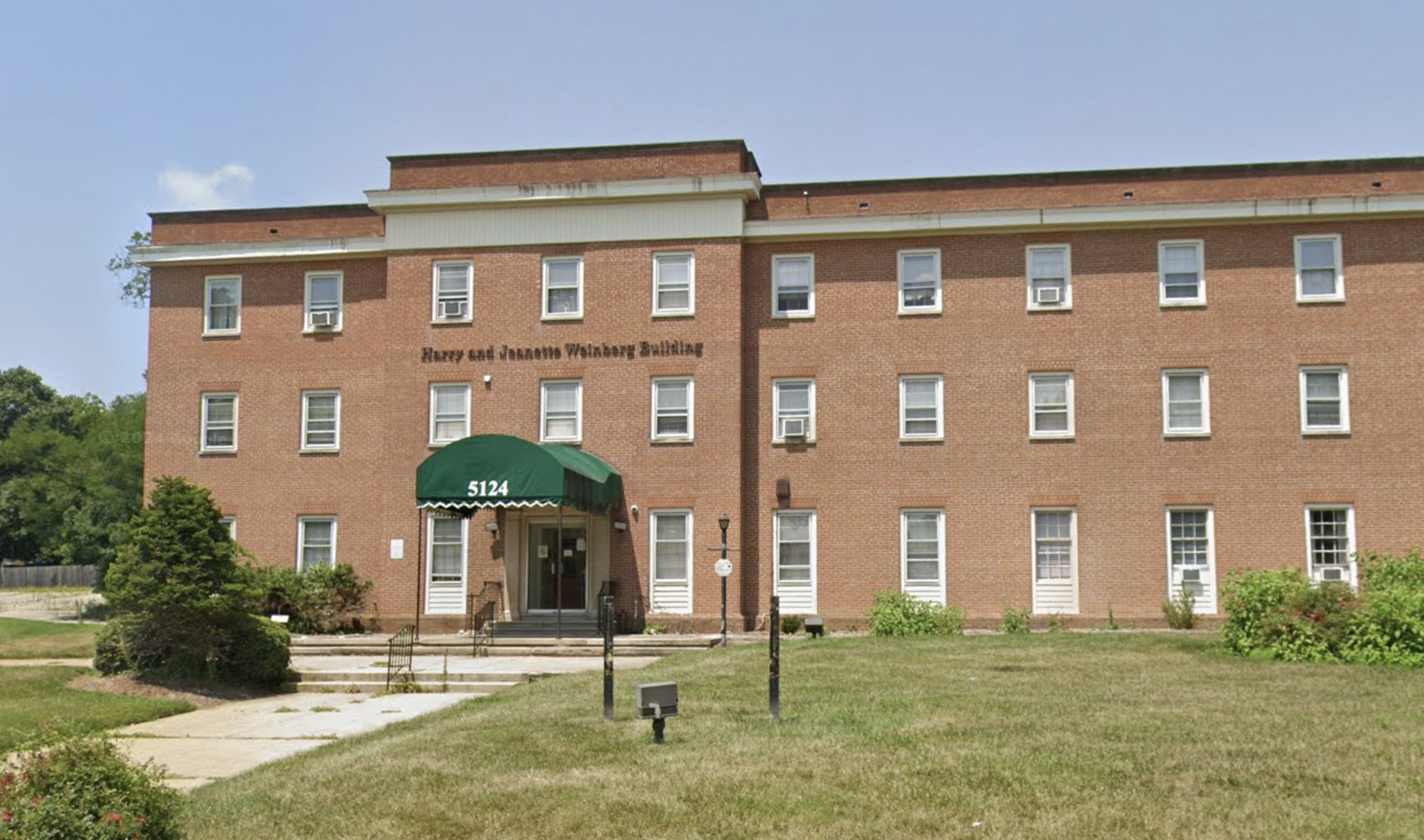 Three-story brick building with a green entrance awning and lawn