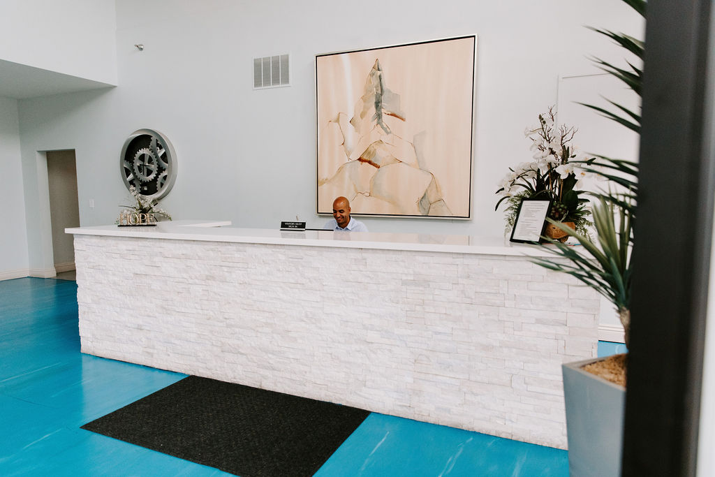 Modern reception desk with white stone facade, blue floor, minimalist décor, and contemporary artwork behind the desk