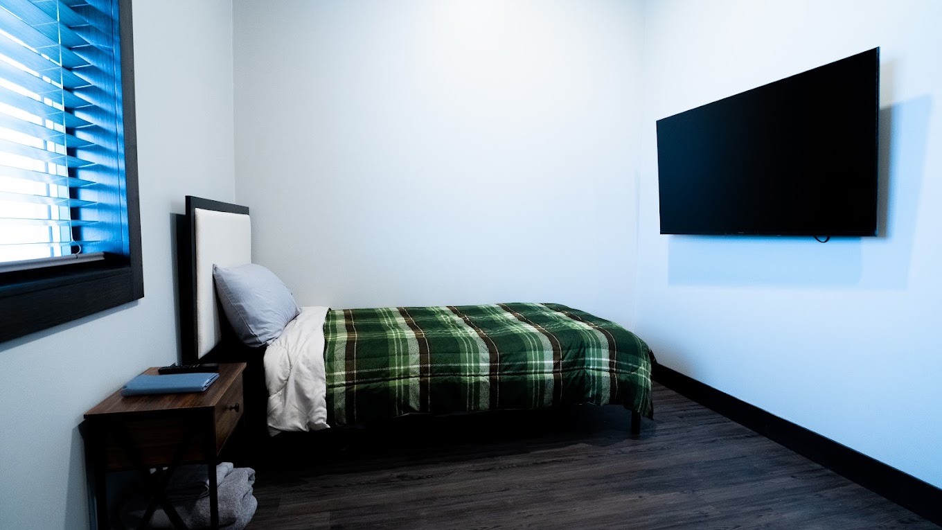 Simple rehab bedroom with a single bed, TV, and wood flooring.