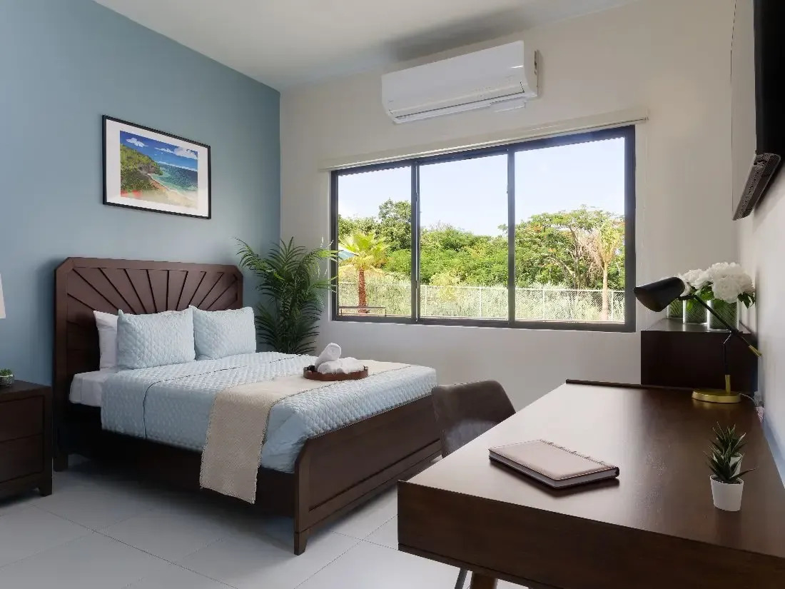 Sunlit bedroom with queen bed and large window overlooking trees.