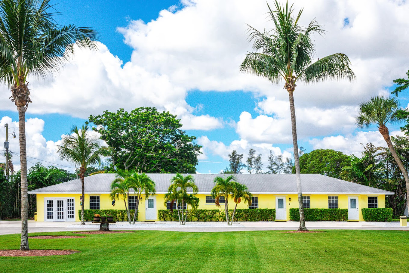 Yellow rehab facility with palm trees and lawn.