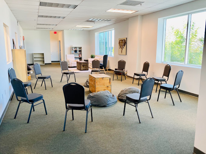 Large, well-lit room with chairs arranged in a circle and bean bags, perfect for group therapy and interactive activities.