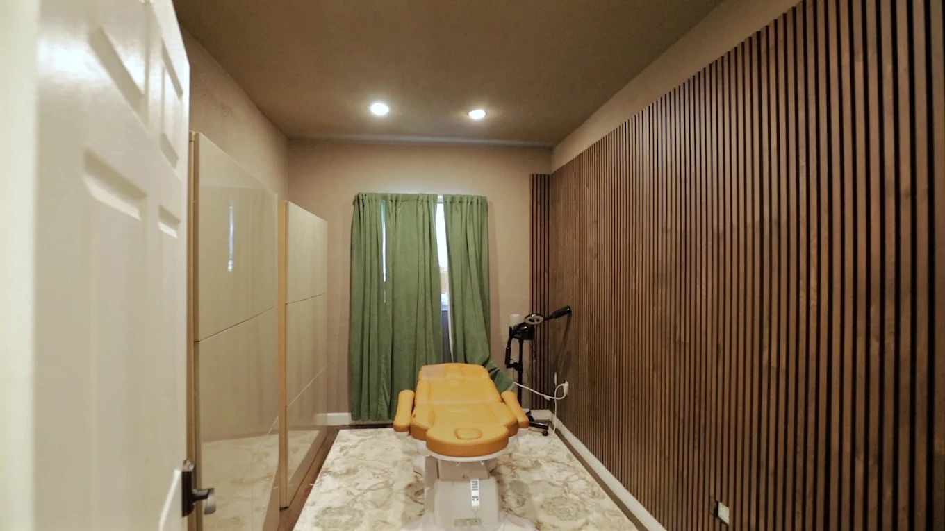 Private treatment room with an adjustable exam chair, privacy partitions, green curtains, and wood slat accent wall