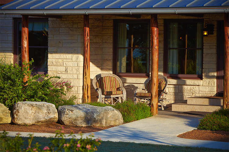 Wicker chairs on a shaded stone cabin porch