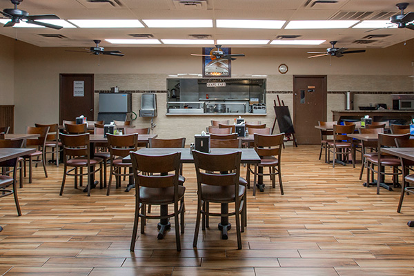 Spacious dining hall with wooden tables and chairs facing open kitchen