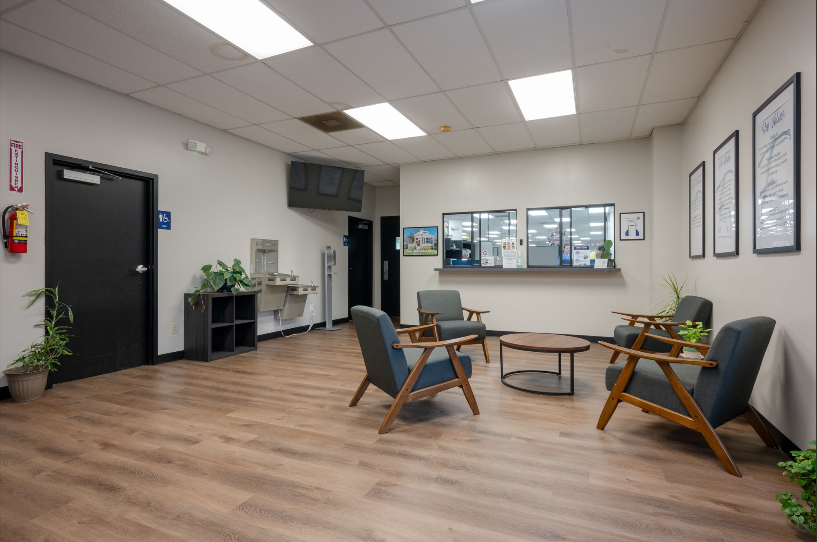 Spacious waiting area with modern chairs, reception window, and plants