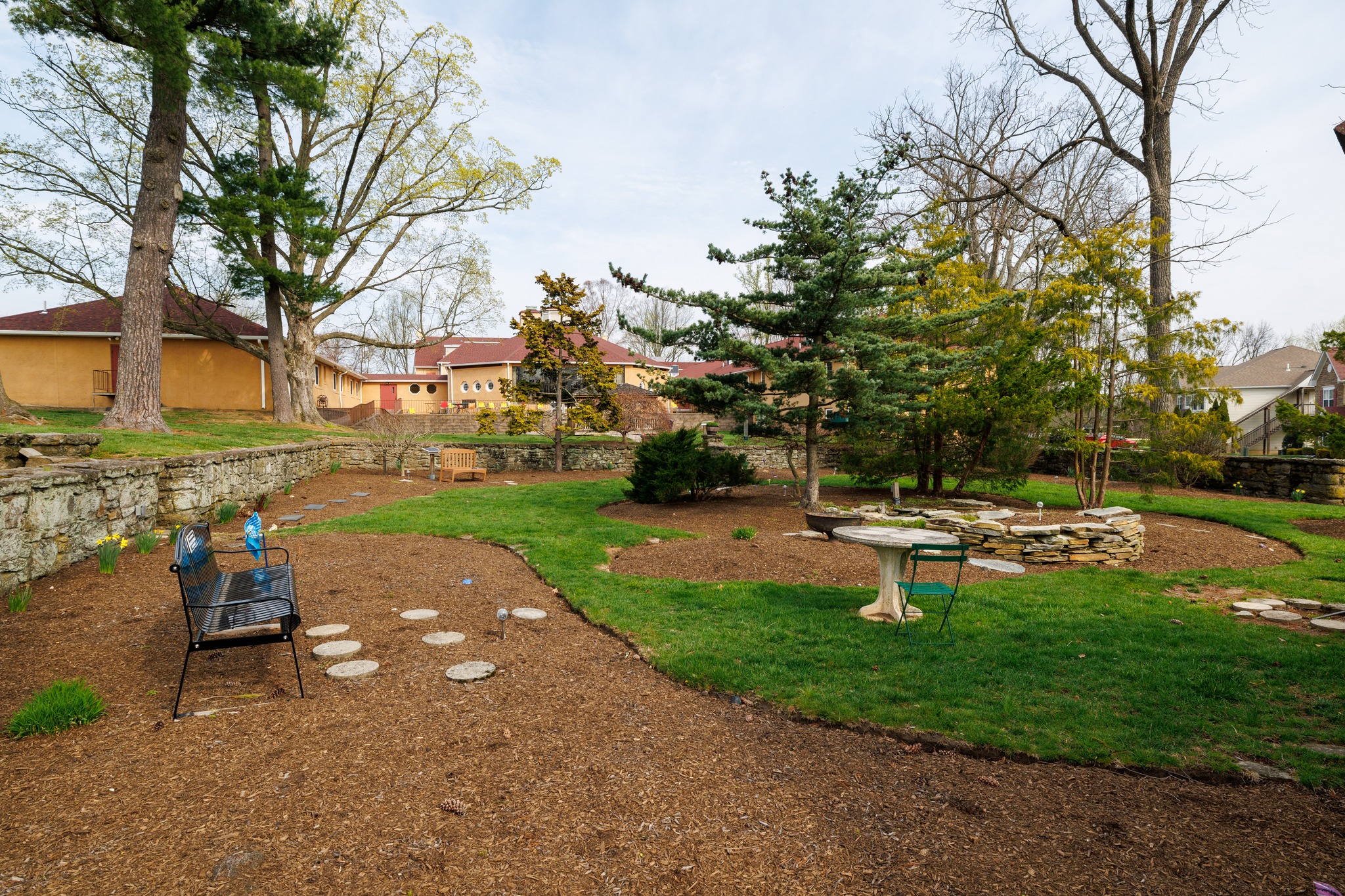 Garden with benches, stone path, and trees near campus buildings