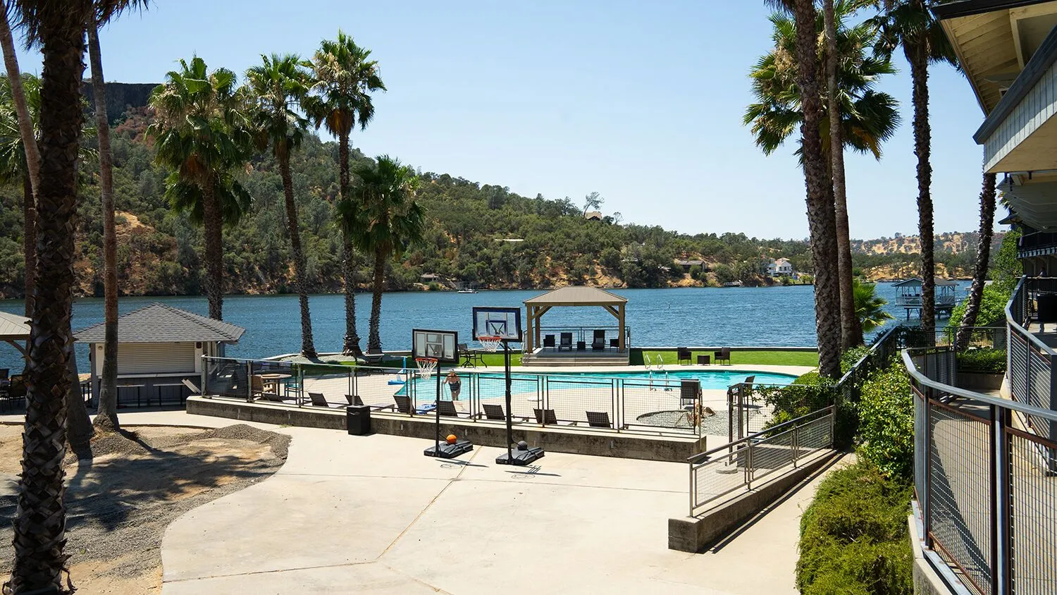 Outdoor basketball hoops beside pool and scenic lakeshore.